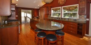 An photo of a kitchen in all cherry wood, with a round marble top table surrounded by barstools.